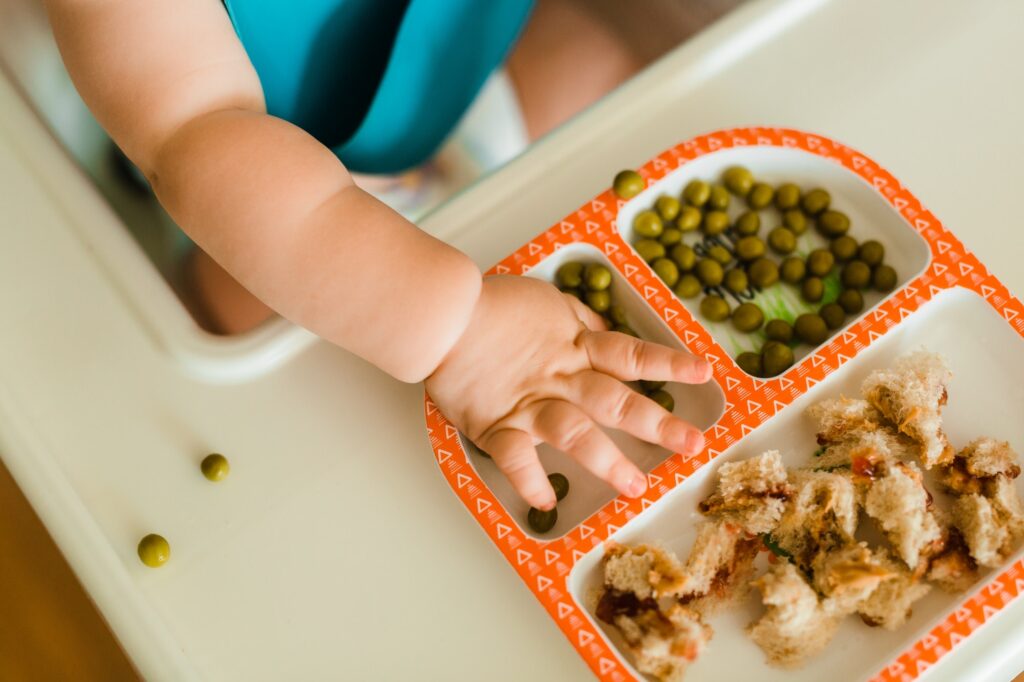 Cute kid eats peas for dinner while inside at home.